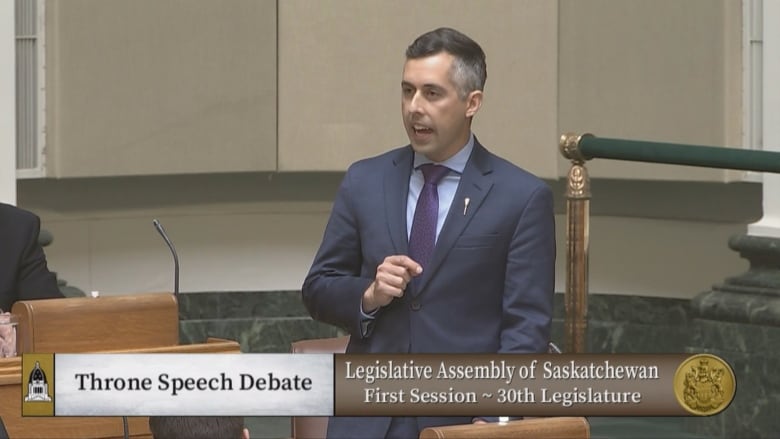 A screenshot from television shows a man in a suit speaking and gesturing.