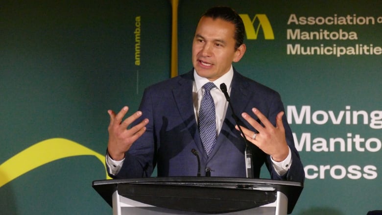 A man in a suit gestures with both hands while speaking at a podium.