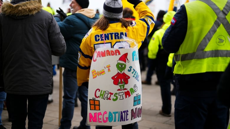 A woman in a crowd wears a sign with a drawing of the Grinch. It reads 