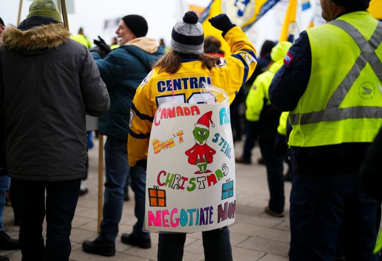 A woman in a crowd wears a sign with a drawing of the Grinch. It reads 