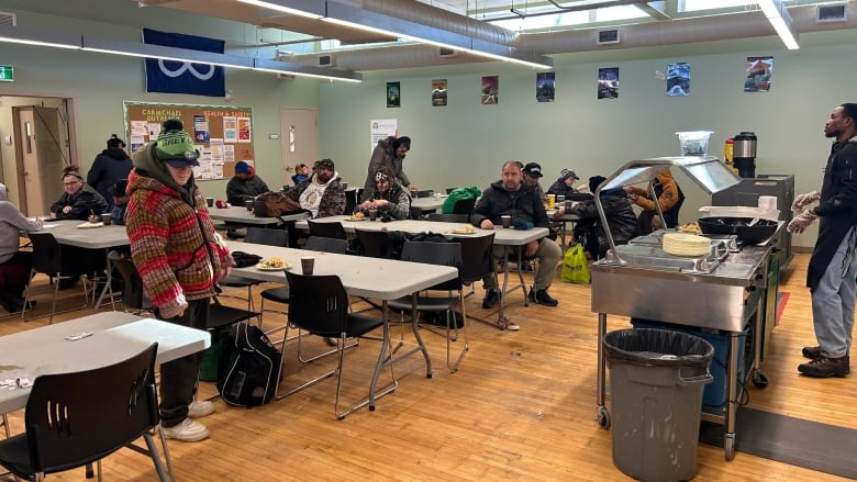 People in a large room sitting at folding tables and some are eating.