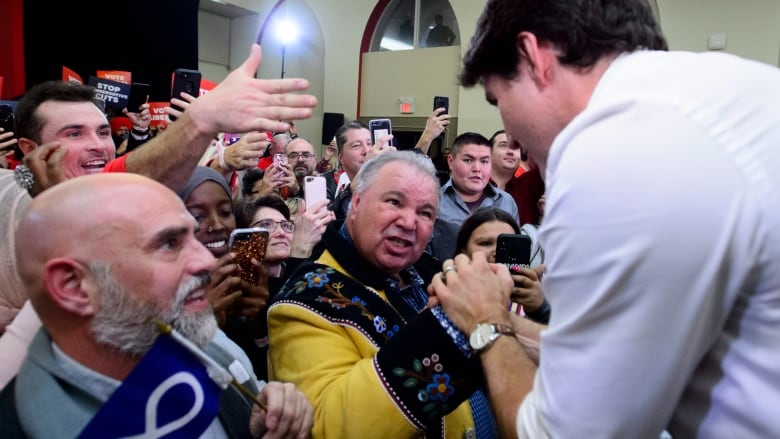 A man grabs the hand of another man in a crowd of cheering people.