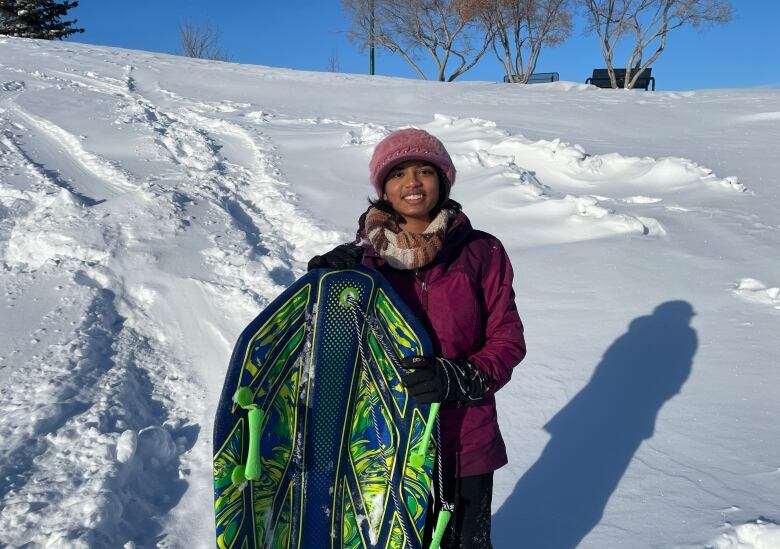 A child holds a snowboard in front of a snow covered hill.